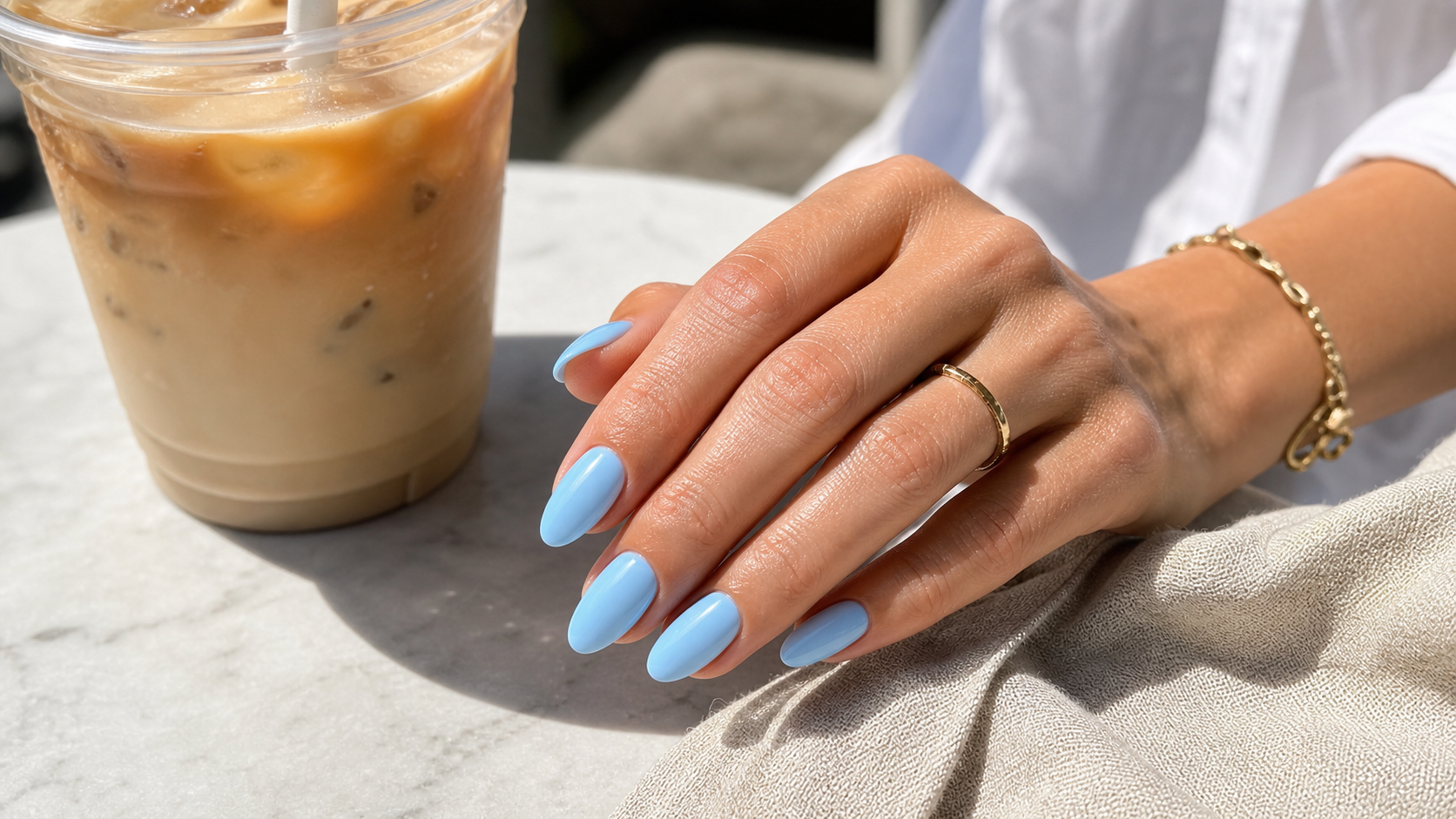 Sky blue gel nails in a clean summer cafe setting with an iced coffee and pale linen