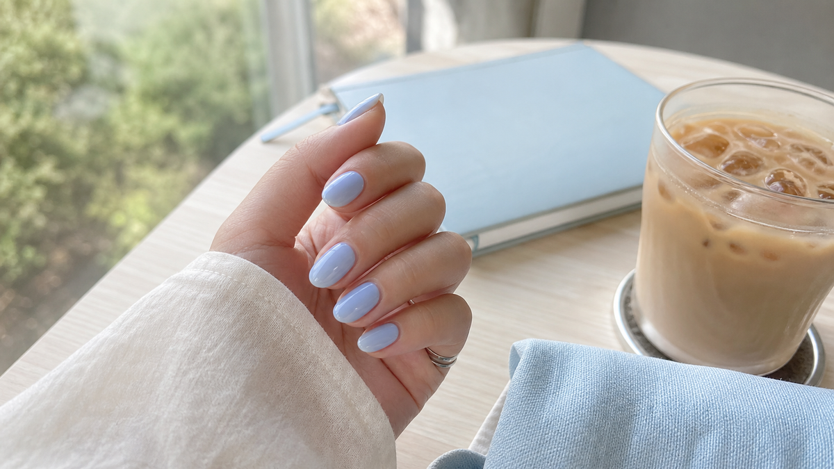 Blueberry milk nails summer manicure with glossy sheer blue nails beside an iced latte and pale blue notebook in soft daylight