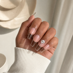 Clear nail extensions with a sheer nude base and rhinestone nail art